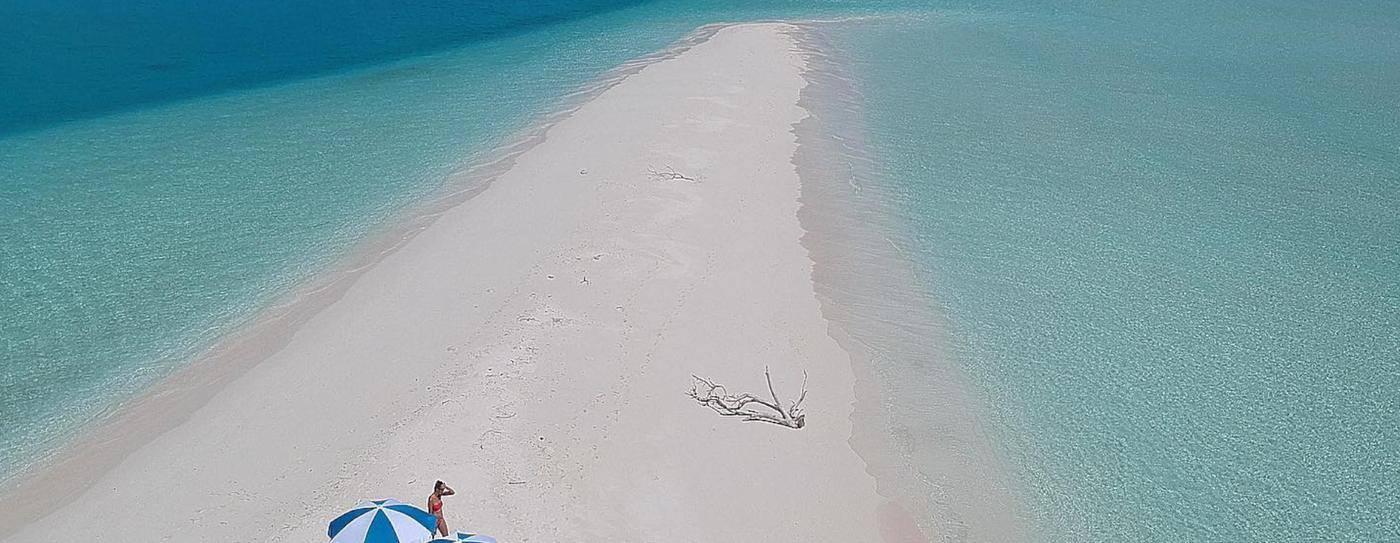 White sandbank surrounded by turquoise water, with a beach umbrella